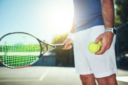 Meet me on the court. Cropped shot of an unrecognizable male tennis player holding a tennis ball and...