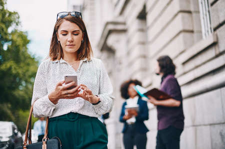 Being connected on the go means you never miss any opportunities. Shot of a businesswoman using her cellphone while out in the city.の写真素材