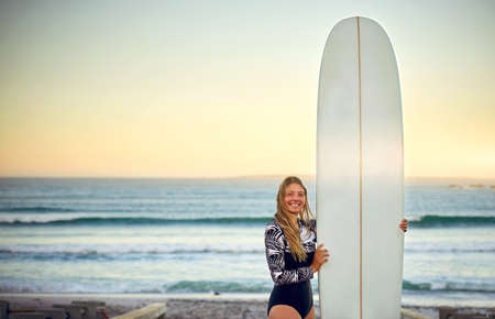 All I need is my surfboard. Cropped portrait of an attractive young female surfer standing with her...