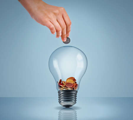 Electricity eating up your savings. Studio shot of a womans hand putting money into a lightbulb.