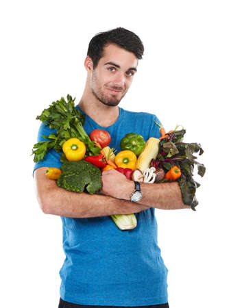 I keep good food close. Studio portrait of a handsome young man posing with a variety of fresh vegetables against a white background.の写真素材
