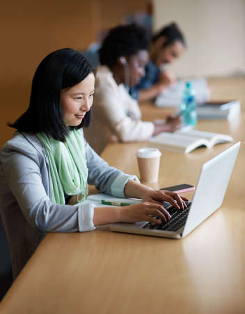 Working on her assignment. A young woman on a laptop in the library.