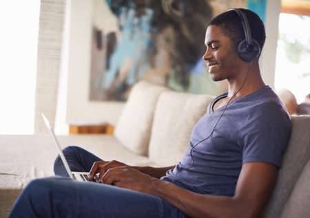 Technological relaxation on the weekend. Cropped shot of a handsome young man using his laptop while...