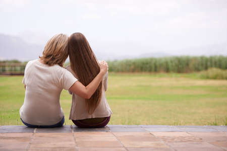 These moments together are so precious. An affectionate mother sitting outside with her adult daughter.の写真素材