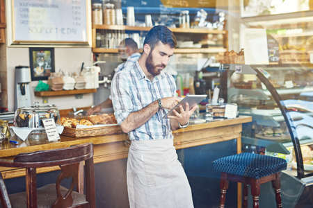 Creating a presence on social media. Shot of a young man using a digital tablet while working in a coffee shop.の写真素材