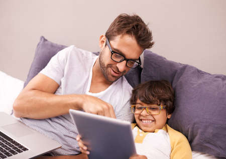 Thats my favorite. Father and son lying on bed while using a laptop and a digital tablet.