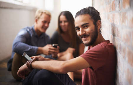 Contacting someone special after class. Shot of three students relaxing in the hallway.