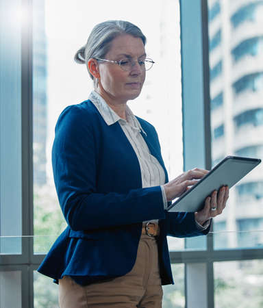 Staying on top of business. Shot of a mature businesswoman using a digital tablet at work.の写真素材