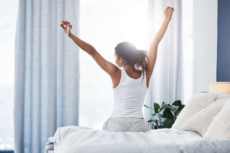 Its a good morning to me. Rearview shot of an unrecognizable young woman stretching while sitting on...