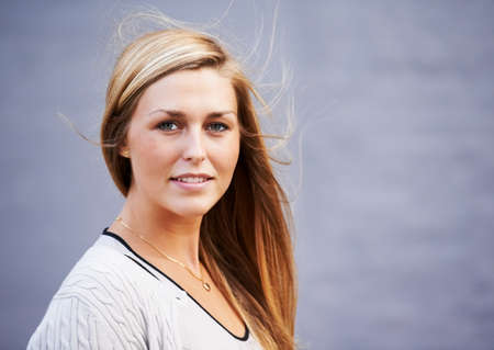 Girl-next-door charm. Portrait of beautiful young woman posing outdoors against a gray background.