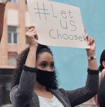 Let us choose. Cropped shot of an attractive young woman holding up a sign protesting against the...