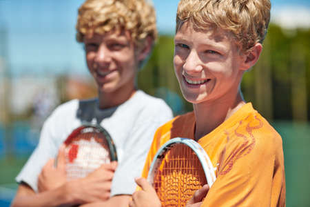 Tennis is their sport of choice. Two friends standing together and holding their tennis rackets on the court.の写真素材