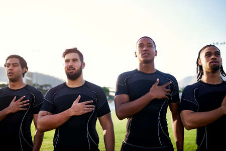 Keeping up with traditions. Cropped shot of a diverse group of sportsmen standing together and singing their national anthem before playing rugby.の写真素材
