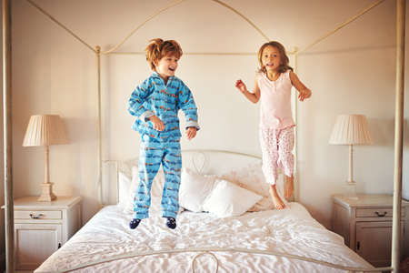 I can jump higher than you. Shot of two young children jumping together on a bed at home.の写真素材