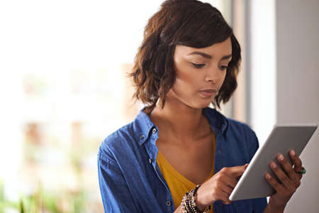 Whats new on the web. Shot of a young woman using a digital tablet at home.