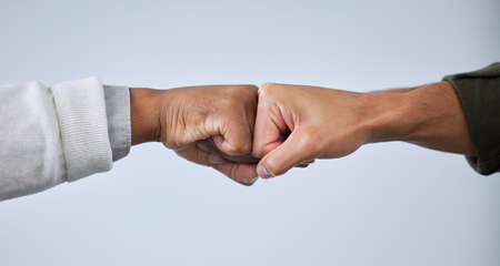 Lets get together and accomplish more. Closeup shot of two unrecognisable men bumping fists against a white background.の写真素材