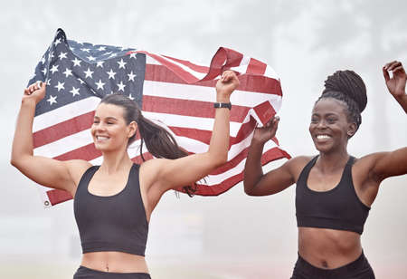 We did this for our country. Shot of female athletes celebrating their win while holding a flag.の写真素材