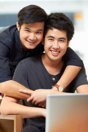 Portrait of an affectionate young gay couple relaxing at home with a laptop.の写真素材