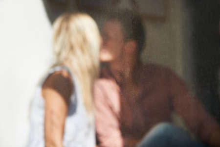 Lost in love. Blurred image seen through a cafe window of a young couple kissing.の写真素材
