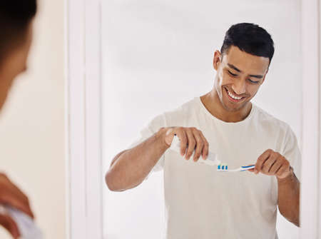 Shot of a handsome young man standing alone in his bathroom and brushing his teeth in the morning.