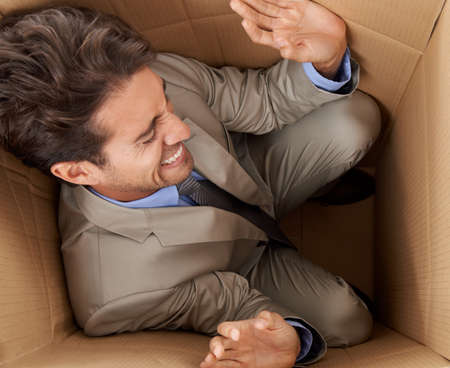 Trapped in his career. Concept shot of a young businessman trapped in a cardboard box.の写真素材