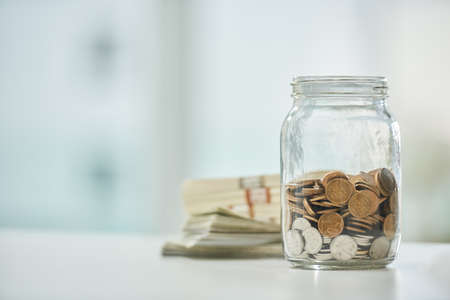 Every penny helps. Full length shot of a jar of coins and wads of cash on a desk in an office.