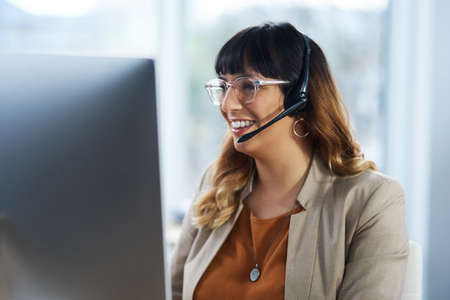Its an absolute pleasure helping you. Cropped shot of an attractive young businesswoman sitting and using a headset in her office during the day.の写真素材