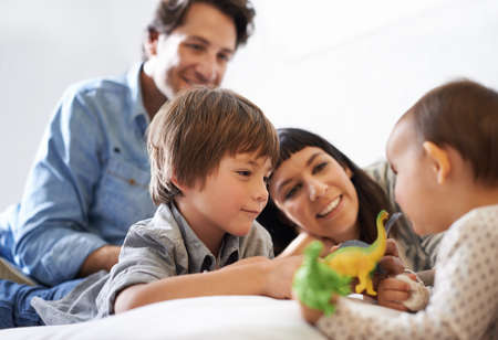 Big brother bonding. Shot of a happy brother and sister playing with their toys while their parents look on.の写真素材