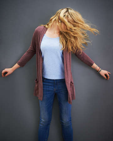 Let your hair down. Shot of a young woman standing against a gray background.の写真素材