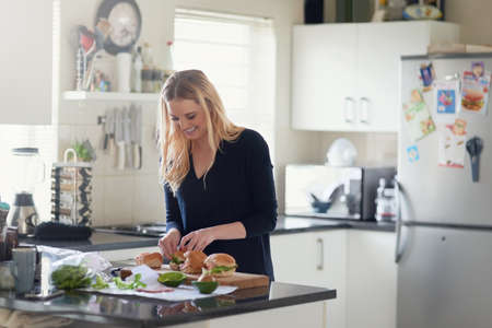 Burgers packed with the goodness of fresh ingredients. Shot of an attractive young woman preparing a meal at home.の写真素材