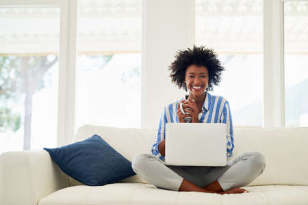 Coffee is my best companion. Portrait of a young woman drinking coffee while working on her laptop...