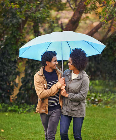 Taking a rainy day stroll. Cropped shot of an affectionate young couple walking under an umbrella.の写真素材