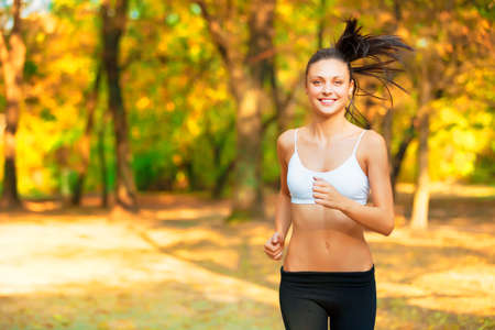 Awesome weather for a run. Shot of a positive-looking young woman jogging in a park in autumn.の写真素材