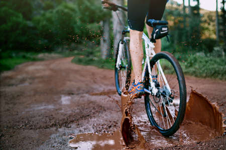 Powering through the mud. Cropped shot of a male cyclist riding along a muddy mountain bike trail.の写真素材