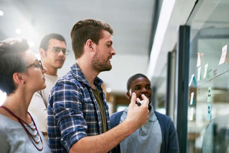 Hes making sure his plans are heard. Shot of a group of designers brainstorming with notes on a...