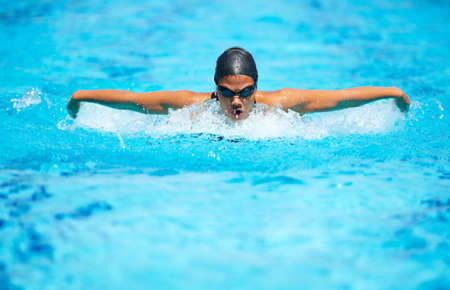 Bettering her time stroke by stroke. A focused young female swimmer doing the butterfly stroke.の写真素材