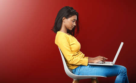 Deep in the world wide web. Studio shot of an attractive young woman using a laptop against a red background.の写真素材