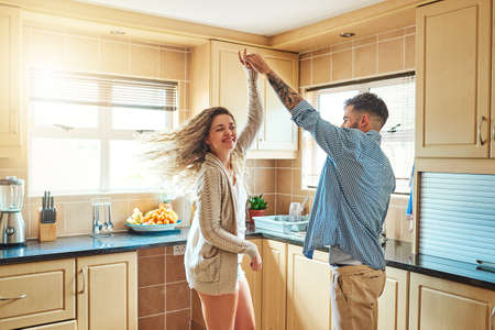 We enjoy the simple things. Shot of a young couple dancing in the kitchen at home.の写真素材