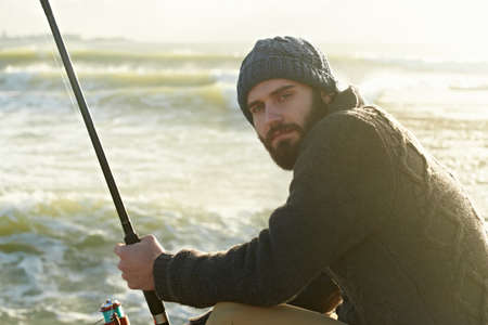 Fishing is his favourite hobby. Cropped shot of a bearded man fishing on the beach.の写真素材