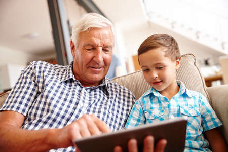 Exploring the web together. Shot of a little boy and his grandfather using a digital tablet at home.の写真素材
