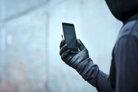 Having a quick look at where Ill strike next. Shot of a male burglar using his phone outdoors.の写真素材