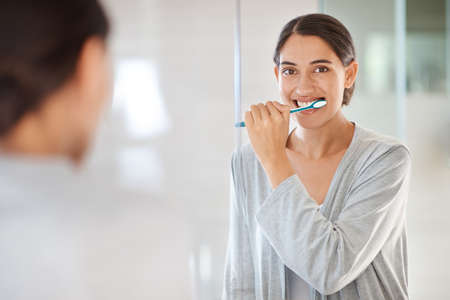 Taking care of her smile. A young woman brushing her teeth.の写真素材
