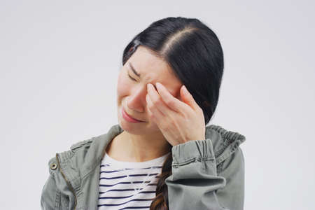 I have something in my eye. Studio shot of a young woman crying while standing against a gray background.の写真素材