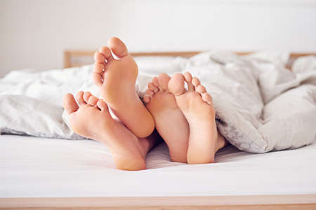 Lets just stay in bed today. Shot of a couples feet poking out from under a duvet.の写真素材