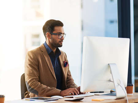 Focused on making his ideas work. Cropped shot of a young businessman working on a computer in an office.の写真素材