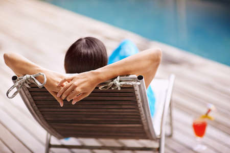 Isnt this the life.... Rear-view shot of a young woman relaxing on a deck chair by the poolside.