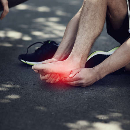 No pain, no gain. Cropped shot of an unrecognizable man suffering with foot cramp during a run.の写真素材