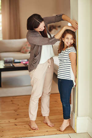 My little girl is growing up so fast. Shot of a beautiful mother measuring her adorable daughters height at home.の写真素材