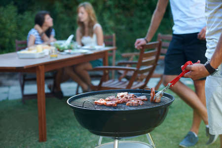 The perfect summer lunch. Young guys barbecuing meat on the grill outdoors - Lifestyle.の写真素材