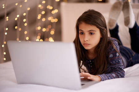 The life of a tween. Cropped shot of a cute little girl using her laptop while lying on her bed.